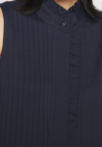 Námořnická modrá blůza s vertikálními proužky, volánkovým výstřihem, zapínáním na knoflíky a jemným leskem, s hladkou strukturou.