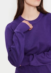 Lila långärmad tröja med ribbad rundhalsning, texturerad tyg och lätt puffade ärmar. Avslutande detaljer på ärmarna med åtsittande manschetter.