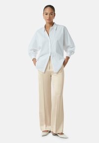 Witte oversized button-up blouse met lange mouwen, gecombineerd met beige wijde broek en lichtgekleurde instappers.