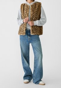 Leopardenmuster-Faux-Fur-Weste mit weicher Textur, kombiniert mit hellblauem, weit geschnittenem Denim-Jeans. Lässiger Look mit einem Kapuzenpullover darunter.