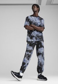 Sæt i sort og blå med mønster, der inkluderer en kortærmet trøje og joggerbukser, parret med sorte sneakers med blå detaljer.