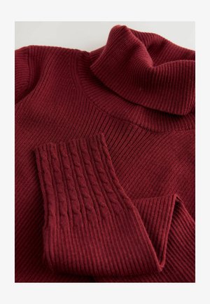 Burgundska rebrasta pletena turtleneck pulover s kablovskim vzorcem na eni rokavu, položen na svetli površini.