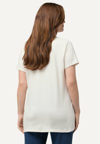 Camiseta de manga corta color crema, de corte holgado, fabricada en algodón suave, con dobladillo redondeado y diseño minimalista, sin patrones ni adornos visibles.