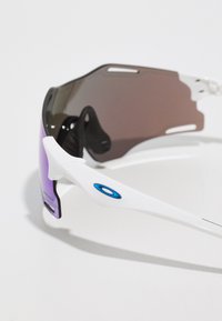 Sportzonnebril met een wit frame, paars-getinte lenzen, gestroomlijnd ontwerp, en een blauwe logoaccent op de poot.