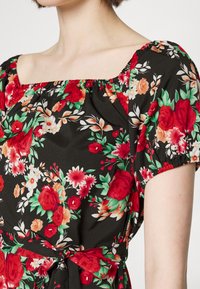 Vestido floral em tecido negro com flores vermelhas, rosas e verdes. Decote quadrado, mangas curtas estilo balão e detalhe de laço na cintura.