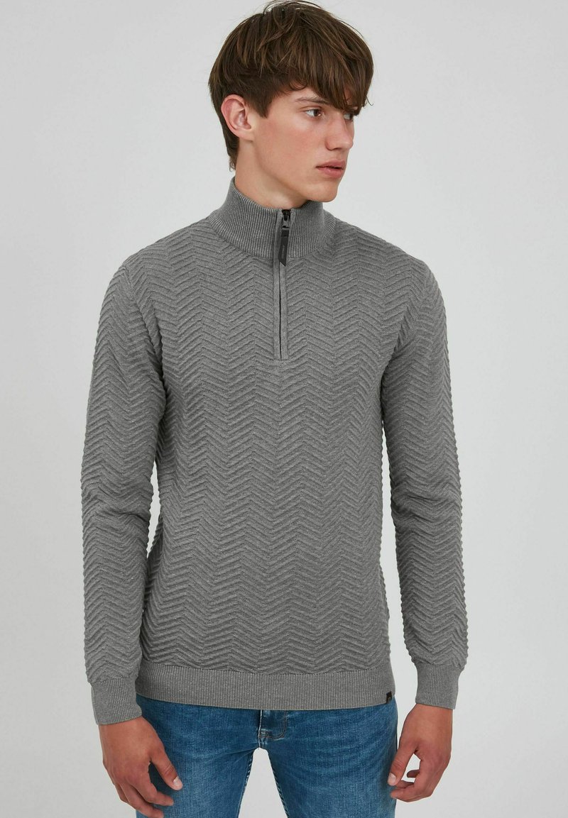 Pull léger gris à col zippé avec un motif en zigzag texturé, des poignets et un ourlet côtelés, et une coupe ajustée. Associe à un jean en denim bleu.
