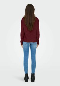 Pull en tricot bordeaux associé à un jean skinny bleu et des bottines noires. Présente un motif texturé et une coupe décontractée.