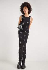 Rochie neagră fără mâneci, cu model din dantelă florală și croială dreaptă. Împreună cu o geantă mică neagră și bocanci negri masivi.