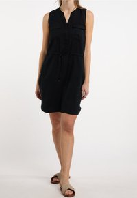 Vestido sin mangas negro con escote en V, frente abotonado, dos bolsillos en el pecho, cintura con cordón ajustable y un corte relajado.