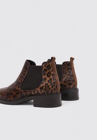 Botas de tobillo con estampado de leopardo, paneles laterales elásticos, acentos de ante marrón y un tacón grueso negro. Textura suave y diseño de punta redonda.