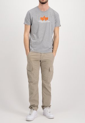 Graues T-Shirt mit kurzen Ärmeln und einem orangen Logo auf der Vorderseite, kombiniert mit beigen Cargo-Hosen mit Seitentaschen und weißen Sneakern.