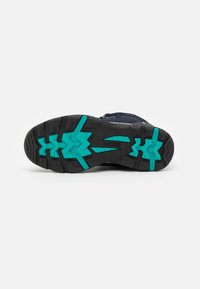 Semelle extérieure de chaussure noire et turquoise avec des crampons profonds et des motifs antidérapants, présentée à plat sur un fond blanc uni.