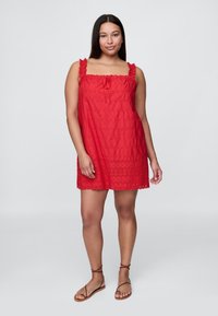 Piros ujjatlan ruha fodros pántokkal, elasztikus nyakkivágással, texturált anyagból és virágmintás lyukacsos szegéllyel. Barna pántos szandállal viselve.