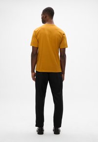 Sininen lyhythihainen t-paita, jossa on pyöreä kaula-aukko, yhdistettynä mustiin housuihin. Tasainen pinta ilman näkyviä kuvioita tai yksityiskohtia.