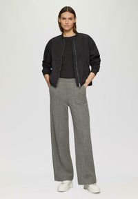 Zwarte bomberjack met ritssluiting, gecombineerd met lichtgrijze wijde broek. Witte platform sneakers maken de look compleet. Zacht materiaal, minimalistisch ontwerp.