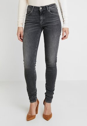 Jeans skinny gris oscuro de denim, con un diseño clásico de cinco bolsillos y un ligero desvanecimiento, combinados con tacones altos marrones.
