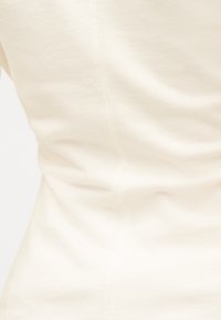 Κοντινό πλάνο μπεζ, λείας υφής υφάσματος με διακριτική κάθετη ραφή και ελαφρές πτυχώσεις, που δείχνει υφή και λεπτομέρειες ραφής.