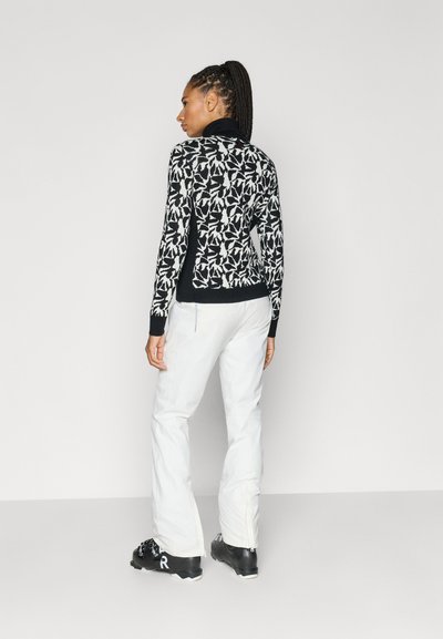 Črno-bela pulover z vzorcem listov, visokim ovratnikom in rebrastimi manšetami, kombiniran z belimi hlačami in črno obutvijo.