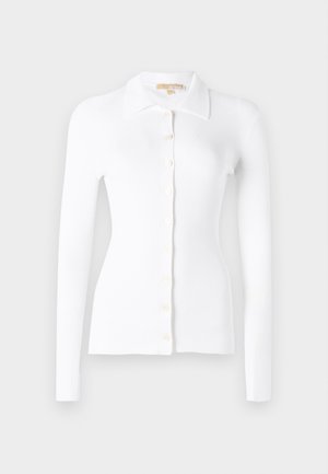 Hvit ripplet cardigan med lange ermer, knapplukking foran, og klassisk krage. Myk tekstur og tettsittende design. Fremtredende knappdetaljer.