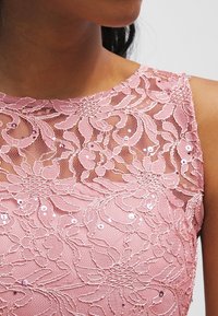 Robe en dentelle rose ornée de motifs floraux avec des sequins, un col haut et un design texturé, mettant en valeur des détails intricats.