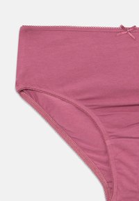 Rosa bomullstrusa med jevn tekstur og elastisk midjebånd. Har en dekorativ sløyfedetalj og bølgete kanter.