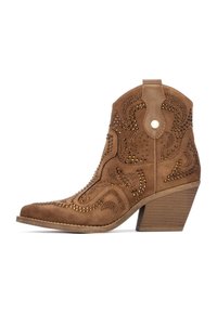 Stivale ankle in suede marrone con punta affusolata, cuciture decorative e dettagli in metallo. Presenta un tacco squadrato e una linguetta per facilitare l'indossamento.