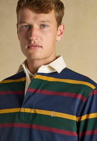 Marineblaues Poloshirt mit grünen, gelben und burgunderfarbenen horizontalen Streifen. Verfügt über einen weißen Kragen, eine Knopfleiste und ein gesticktes Logo auf der Brust.