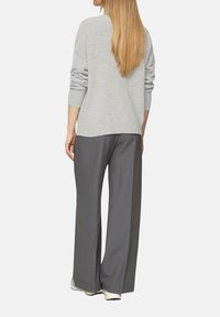 Hellgrauer, übergroßer Pullover mit überschnittenen Schultern, kombiniert mit weit geschnittenen, dunkelgrauen Hosen, beide aus sanften Materialien und in lässigem Design.