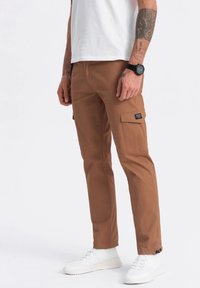 Bruine cargo broeken met een slim fit, voorzien van zijzakken, een labelpatch en een nette afwerking, gecombineerd met witte sneakers en een wit T-shirt.