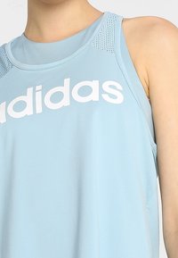 Hellblaues sportliches Tanktop mit Rundhalsausschnitt, Mesh-Einsätzen und einem großen weißen "adidas"-Logo auf der Vorderseite. Weicher, atmungsaktiver Stoff.