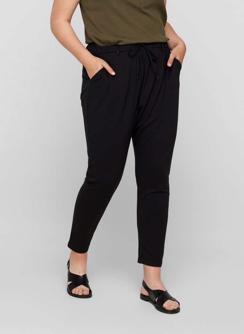 Pantaloni neri a gamba affusolata con elastico in vita e cordoncino, dotati di tasche laterali e una texture liscia, abbinati a sandali neri.