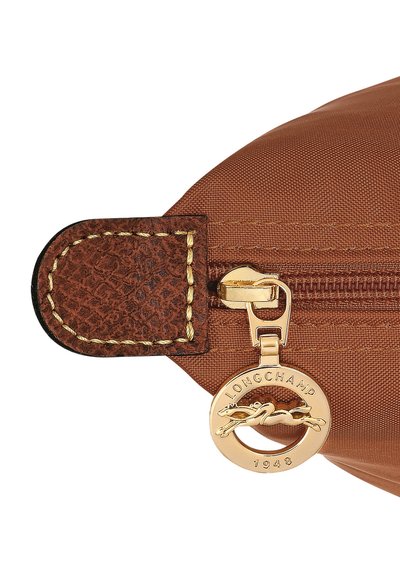 Braune Nylontasche mit einem Reißverschluss-Anhänger aus strukturiertem Leder. Verfügt über goldfarbene Beschläge und einen runden Logoanhänger mit der Gravur "Longchamp 1948".