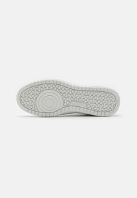 Suela de zapatilla blanca con un patrón de goma texturizado, detalle de diseño circular y nombre de la marca en relieve. Bisel suave con un acabado duradero.