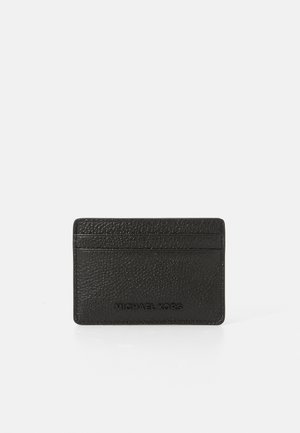 Porte-cartes en cuir noir avec une surface texturée, comportant quatre fentes pour cartes et un logo en relief à l'avant. Design minimaliste.