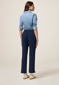 Chemise en denim avec des manches retroussées, associée à un pantalon bleu marine à taille élastique, d'une coupe droite. Des chaussures à enfiler complètent le look.