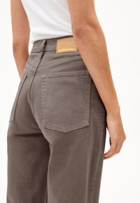 Gray cotton trousers with a high waist, featuring a patch pocket design and a tan leather brand label on the back. Edges stitched.