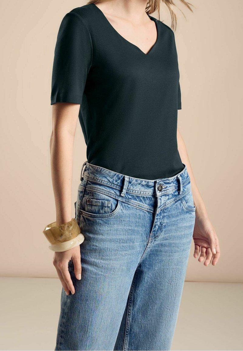 Svart kortärmad V-ringad t-shirt i kombination med ljusblå högmidjade jeans. En framträdande genomskinlig bangle på handleden ger en extra detalj.