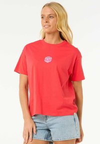 T-shirt en coton corail vif à manches courtes, avec un petit imprimé graphique blanc sur la poitrine, associé à un short en denim.