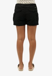 Bermudas negras de corte relajado, con dos bolsillos traseros, bolsillos laterales y una textura suave y lisa. Detalle de cinturilla elástica.
