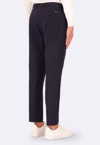 Pantaloni a righe navy in design affusolato, con tasche posteriori e un discreto tag del marchio, abbinati a sneaker bianche.