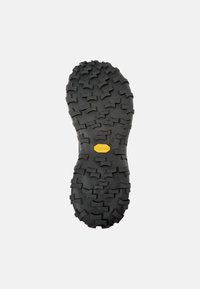 Svart gummisåle med fremtredende multi-retningstagger for grep. Har en gul Vibram-logo i midten.