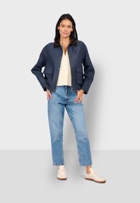 Námořnická bunda s hnědým límcem, s dvěma předními kapsami, zipovým zapínáním a volným střihem. Kombinováno s světle modrými džíny a béžovými teniskami.