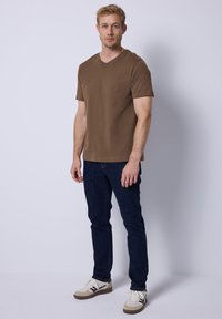Camiseta de cuello en V marrón, de manga corta, combinada con unos vaqueros oscuros y zapatillas blancas con detalles beiges. Diseño sencillo, corte casual.