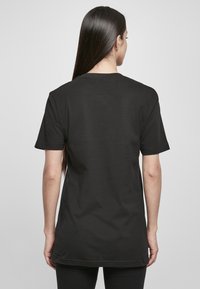Schwarzes Baumwoll-T-Shirt mit Rundhalsausschnitt und kurzen Ärmeln, ausgestattet mit einem geraden Schnitt, der bis zur Hüfte reicht. Keine sichtbaren Grafiken oder Muster.
