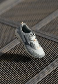 Light gray athletic shoe with mesh upper, rubber sole, orange accents, and black logo detail. Features rounded toe and lace-up design.