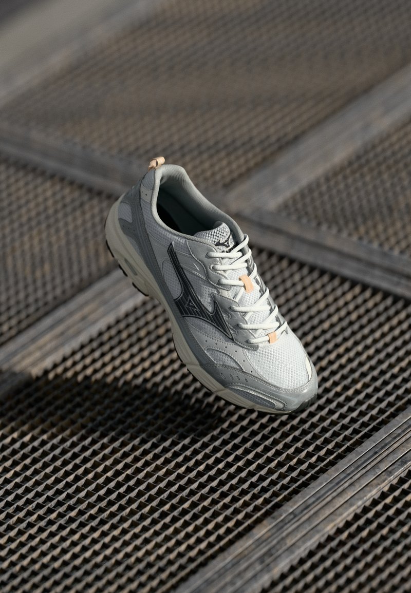 Light gray athletic shoe with mesh upper, rubber sole, orange accents, and black logo detail. Features rounded toe and lace-up design.