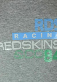 T-shirt grigia con la scritta "RDS RACING REDSKINS & CO84" in blu, verde e grigio; lettering testurizzato con un design grafico sportivo.