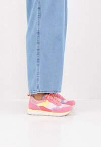 Ροζ και κίτρινα αθλητικά παπούτσια με στρώσεις από σουέτ και πάνελ από δίχτυ, με χοντρή λευκή σόλα και κορδόνια, συνδυασμένα με ανοιχτό μπλε τζιν.