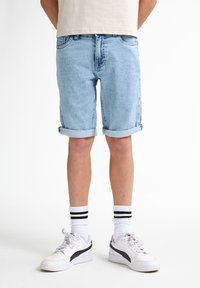 Světle modré denimové šortky s ohrnutými manžetami, designem se pěti kapsami, rovného střihu, doplněné o bílé tenisky a pruhované ponožky.