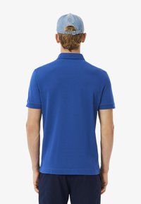 Blå polotröja i slät tyg, med korta ärmar och krage. En ljusblå keps fullföljer outfiten.